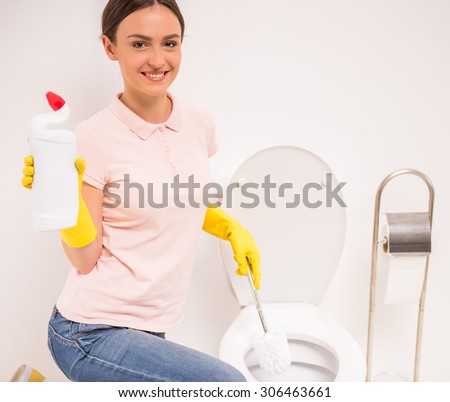 Woman with a rubber glove cleans a toilet bowl using means for cleaning