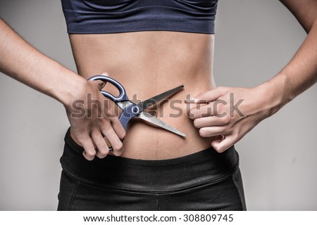 Young skinny woman cuts her belly by scissors. Weight loss concept.