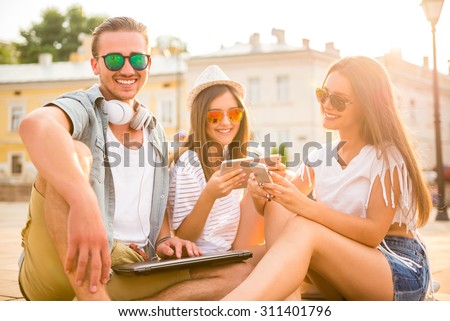 Friendship, leisure and people concept. Young people having a good time together, using digital tablet, sitting outdoors, in the town.