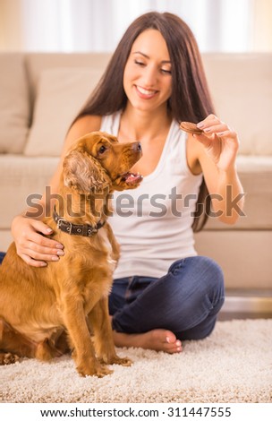 Happy woman is playing with a dog and feeding him sitting on the floor at home.