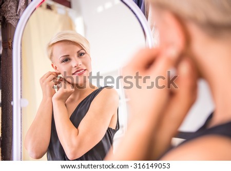 Beautiful young woman putting on her a new earrings and smiling while looking at the mirror.