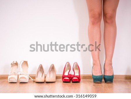 Cropped image of young woman in high heeled shoes standing against the wall while more shoes laying in a row near her