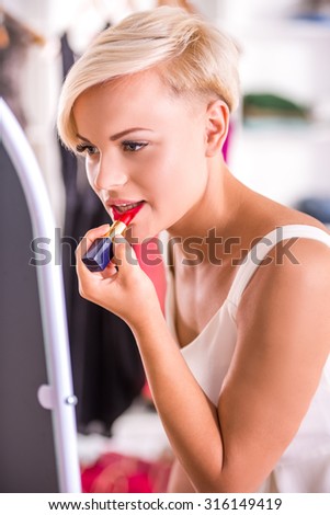 Beautiful young woman is doing makeup, draws lips lipstick.