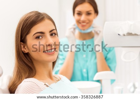 Portrait of a happy patient with braces on the teeth, sitting in the dental chair, in the background a young doctor dentist