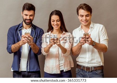 Technology and internet concept: group of young people looking at their smartphones, on a gray background