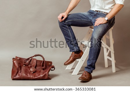 Young business man with a brown leather bag, a white shirt and blue jeans on a gray background
