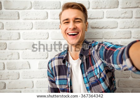 Beautiful young man in casual clothes make selfie on a background of white brick wall