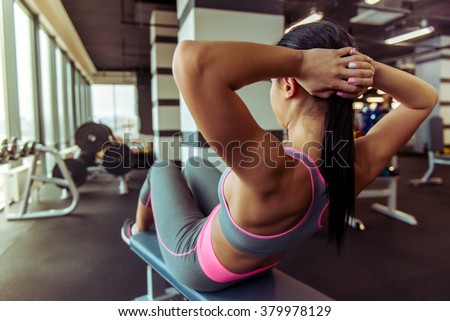 Back view of attractive young woman doing abs while working out in gym