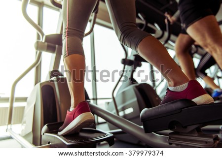 Back view of attractive young people working out on an elliptical trainer in gym