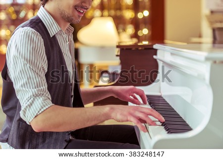 Handsome stylish man in classical vest smiling while playing a piano in a musical shop, cropped