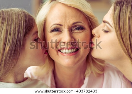 Beautiful granny is looking at camera and smiling while her daughter and granddaughter are kissing her