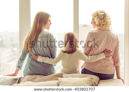 Back view of three generations of beautiful women sitting on sofa against window