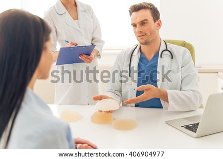 Handsome young doctor is holding a breast implant while giving a consultation to beautiful woman