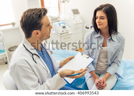 Handsome doctor is talking with young female patient and making notes while sitting in his office