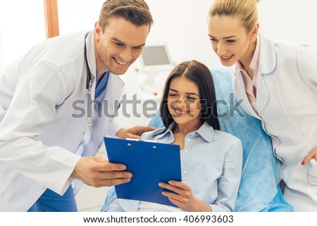 Beautiful female patient and two doctors are looking at folder with documents and smiling, at the doctors office