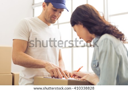 Attractive young woman and handsome delivery worker are signing documents for moving, cardboard boxes in the background