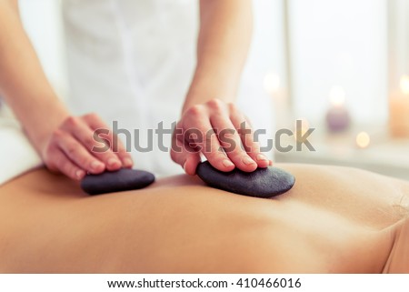Cropped image of massage therapist putting spa stones on the back of beautiful blonde girl lying on a massage table