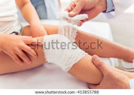 Little girl and her mother at doctors. Handsome middle aged pediatrician is putting a bandage on little girl knee, close-up