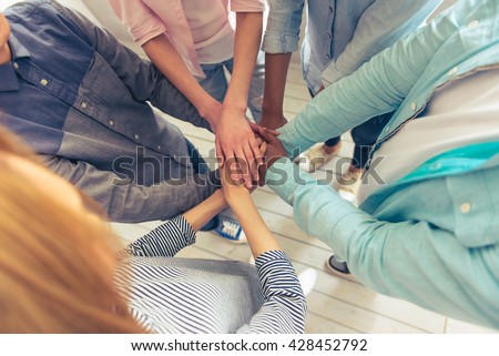 Top view of young business people of different nationalities holding hands together, cropped