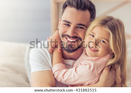 Portrait of handsome father and his cute daughter hugging, looking at camera and smiling