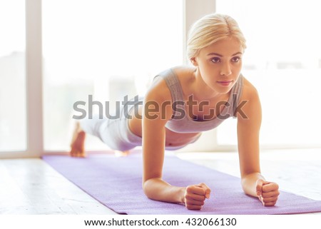 Beautiful young woman in sports wear doing plank exercise on yoga mat