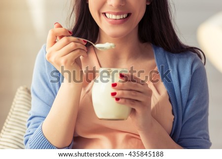 Cropped image of beautiful pregnant woman eating yogurt and smiling while sitting at home