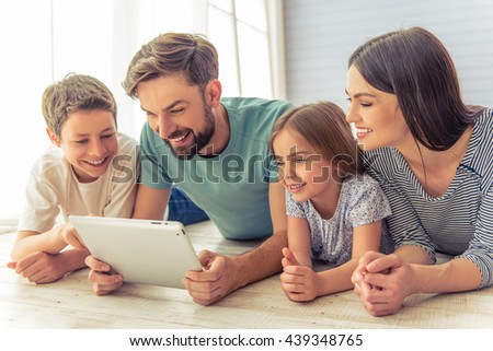 Beautiful young parents, their cute little daughter and son are using a tablet and smiling, lying on the floor at home