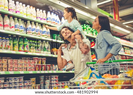 Beautiful young parents and their cute little daughter are smiling while choosing food in the supermarket. Girl is sitting on her dad\'s shoulders