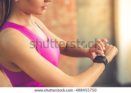 Cropped image of beautiful sports girl is switching on her fitbit before training while standing in fitness hall