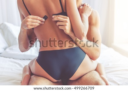 Cropped image of beautiful passionate couple having sex on bed. Man is unfastening bra