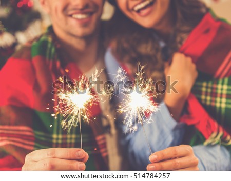 Cropped image of happy young couple holding sparklers, hugging and smiling while celebrating Christmas at home