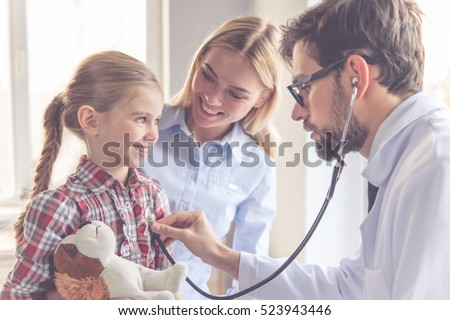 Beautiful young mother and her little daughter at the pediatrician. Doctor is examining little patient using a stethoscope