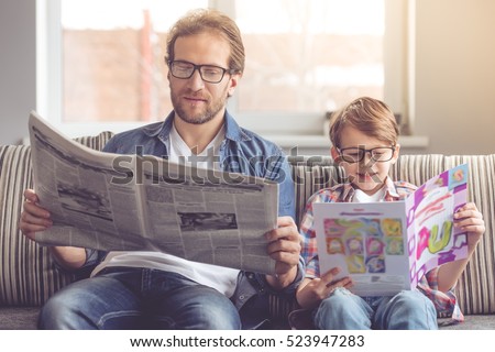 Father and son are reading newspapers and smiling while spending time together at home
