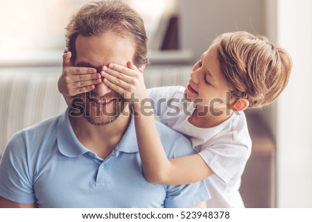 Father and son are smiling while spending time together. Little boy is covering his dad eyes