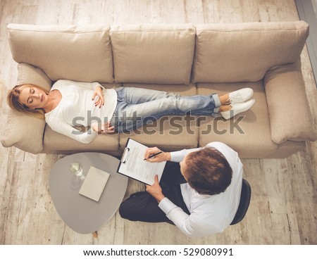 At the psychologist. Top view of beautiful young woman lying on couch while doctor is making notes