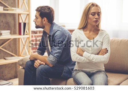 Beautiful couple is sitting back to back on the couch while having a quarrel
