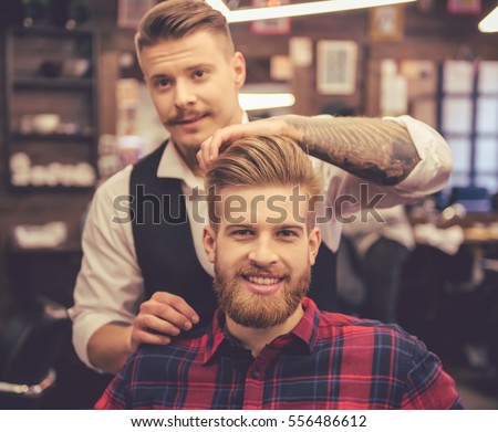 Handsome bearded man is smiling while having his hair cut by hairdresser at the barbershop