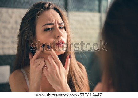 Beautiful girl in white bra is squeezing pimples on her face while looking into the mirror in bathroom