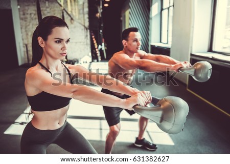 Beautiful young sports couple is working out with kettlebell in gym