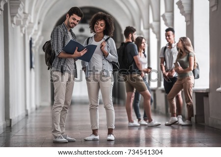 Beautiful young students are resting in university hall, a couple in the foreground is studying something and smiling