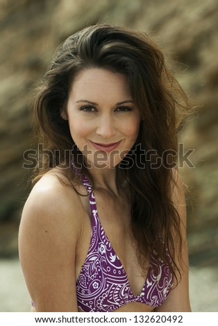 Relaxed attractive brunette girl wearing purple bikini poses on the rock by the sea. Evening soft light at coastline of Rancho Palos Verdes, CA.
