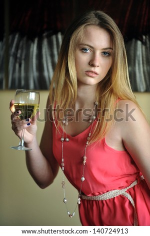 Portrait of young blond girl holding glass with white vine at natural light from window