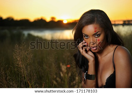 Beautiful African-american woman wearing black lingerie corset at the sunset at grass field during sunset time