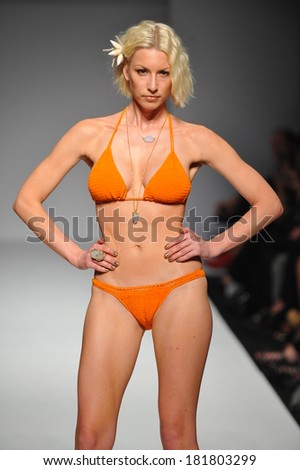 Attractive bikini model walking the runway wearing bright color swimsuit and flower in the hairs.
