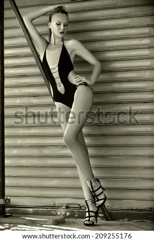 Brunette swimsuit model posing sexy outdoor in front of metal gate.Black and white picture.
