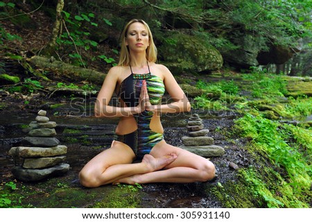 Young woman meditating in lotus posture, doing yoga in the forest nature.