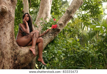 Portrait of beautiful African American woman sitting on the tree and enjoying spring flowers in the tropical forest