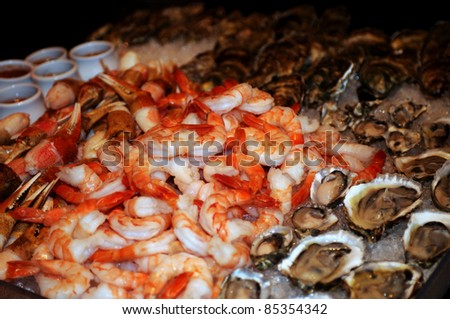 tray of piled stone crab claws, raw jumbo shrimps and oysters on ice with hot sauce