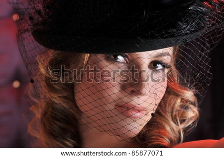 Closeup portrait of sexy lingerie model posing pretty at studio vintage background set and wearing black tight bra and small retro style designer\'s hat