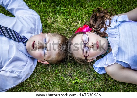Young brother and sister lay down in the grass dressed up close their eyes relaxing in the grass outside
